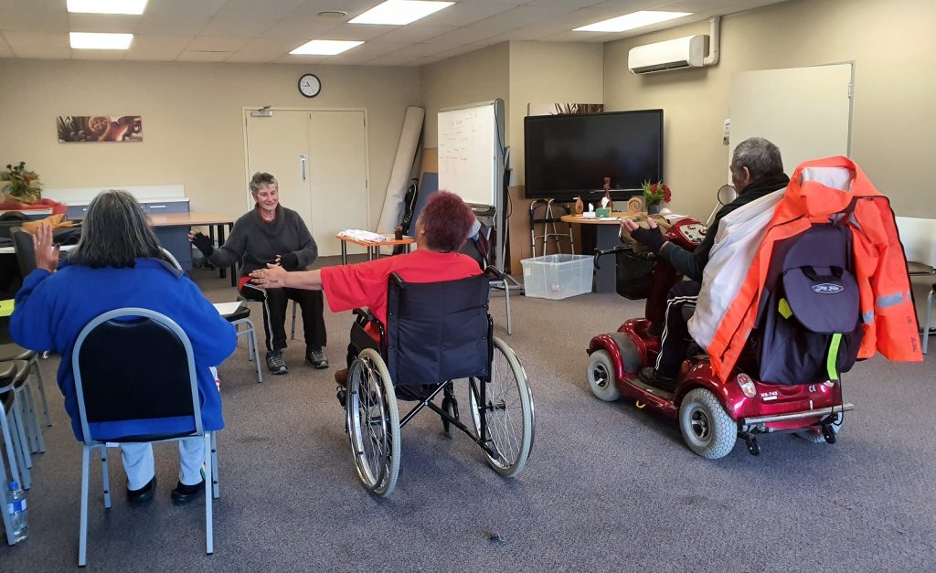 Four seated people doing tai chi. One is seated in a wheelchair and another in a shiny, red mobility scooter