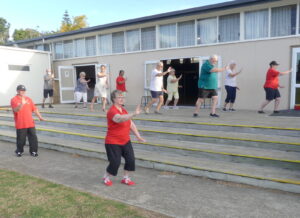 Group of people doing tai chi on the outdoor deck of a hall