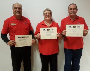 Three people wearing red shirts, all smiling and holding up their certificates