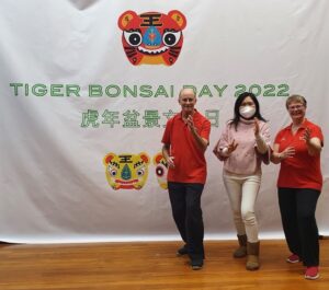 Three people doing a tai chi pose against a big banner that reads in Chinese and English letters: "TIger Bonsai Day 2022)