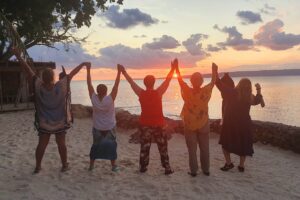 Group of people raising their arms in celebration with the sunset in the background.