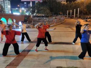 Group of people doing tai chi in an outdoor area at night, with outdoor lighting