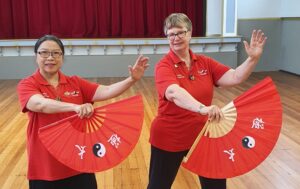 Two women in red shirts doing holding red tai chi fans